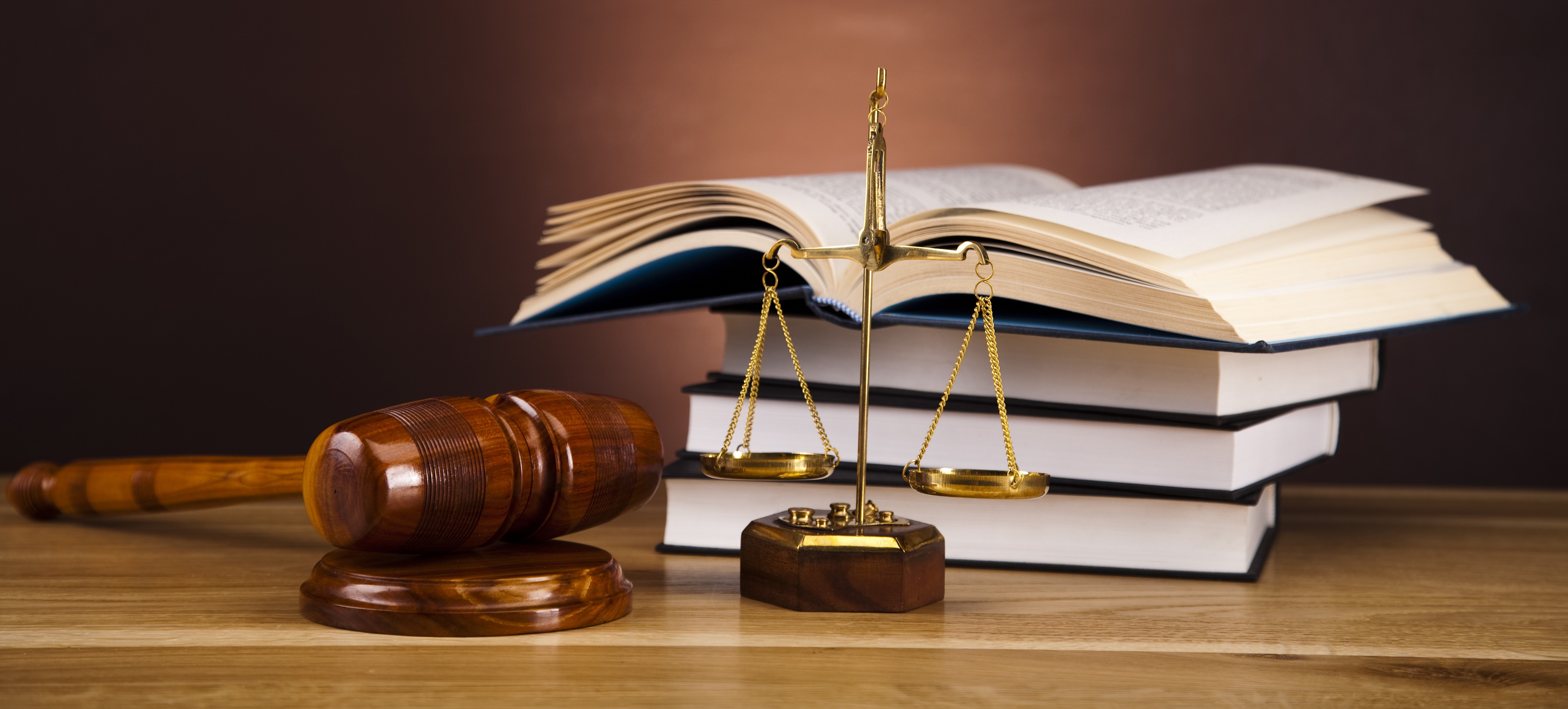 Books, a gavel, and scales of justice pictured on a desk.